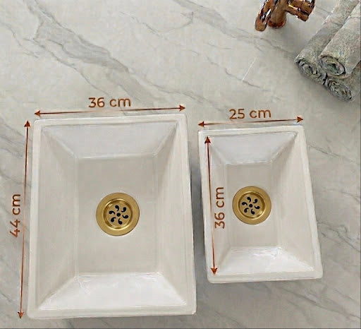 Vue de dessus de deux vasques rectangulaires artisanales en céramique blanche brillante posées sur un plan de travail en marbre gris. Des flèches indiquent les dimensions : le grand modèle mesure 44 x 36 cm et le petit modèle mesure 36x25 cm. Une robinetterie en laiton brossé est visible dans le coin supérieur.